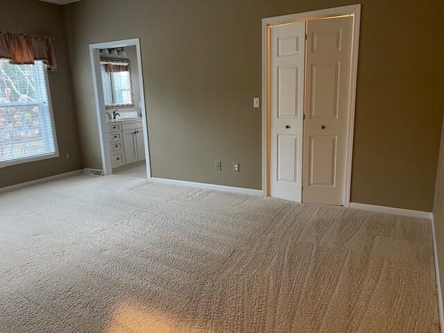 unfurnished bedroom featuring light carpet, ensuite bath, and baseboards