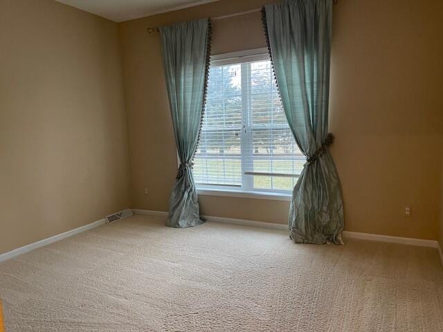 empty room featuring carpet floors, plenty of natural light, visible vents, and baseboards