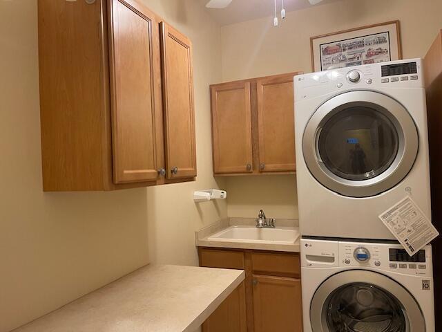 washroom featuring a sink, cabinet space, ceiling fan, and stacked washer / drying machine