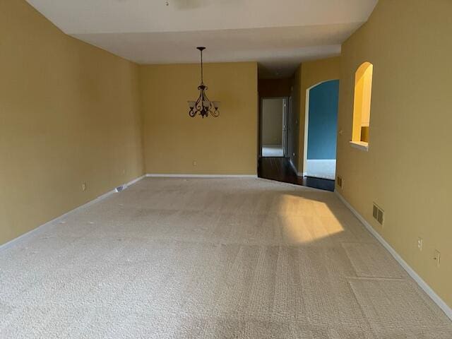 carpeted spare room with baseboards, arched walkways, visible vents, and an inviting chandelier