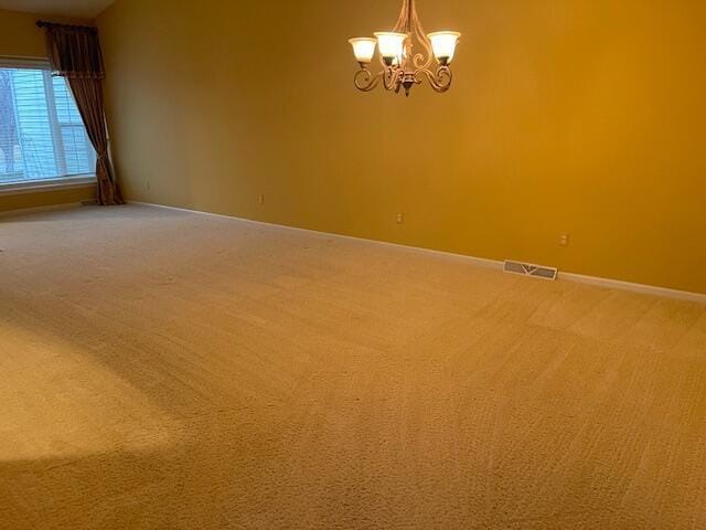 carpeted empty room with baseboards, visible vents, and an inviting chandelier