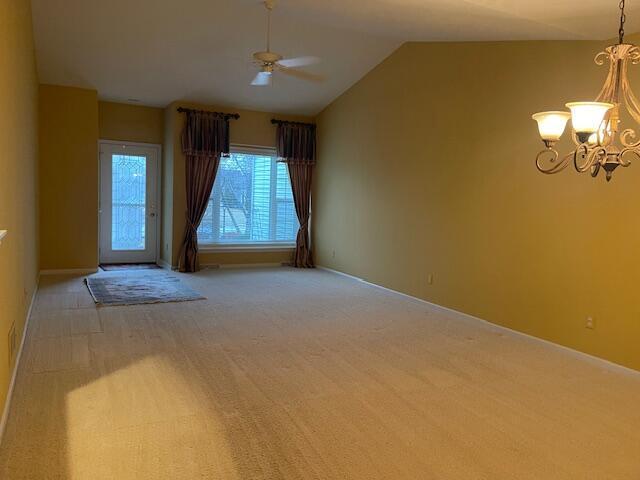 empty room featuring lofted ceiling, light colored carpet, and ceiling fan with notable chandelier