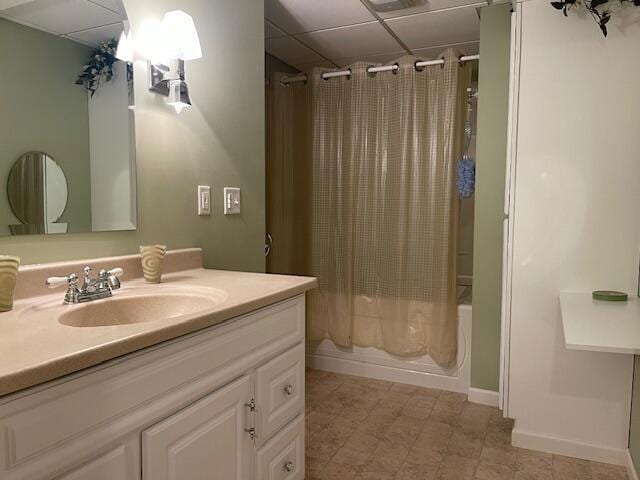 bathroom featuring a paneled ceiling, baseboards, shower / bath combo with shower curtain, and vanity