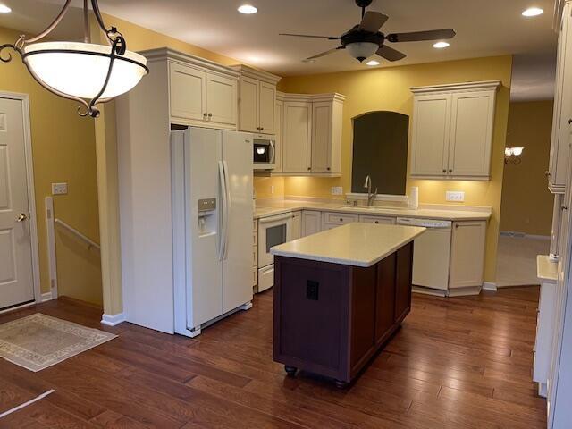 kitchen with a center island, pendant lighting, light countertops, a sink, and white appliances