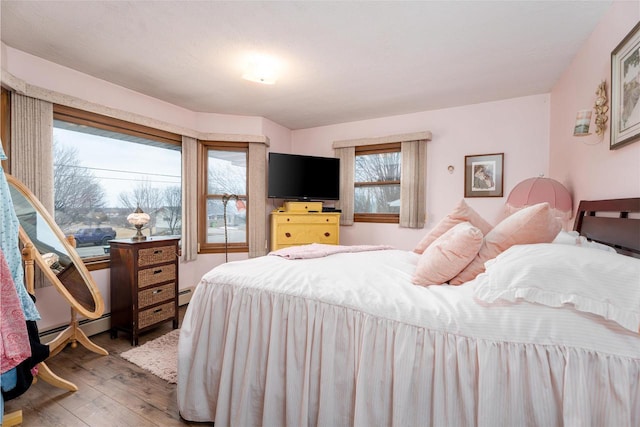 bedroom with a baseboard heating unit and wood finished floors