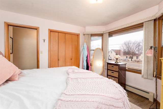 bedroom featuring a baseboard heating unit, a closet, and wood finished floors