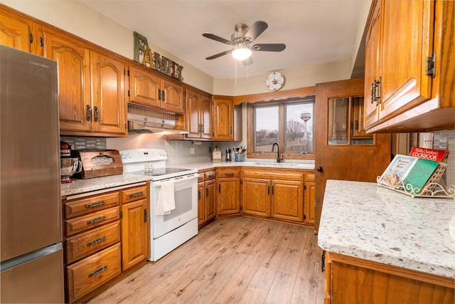 kitchen with white electric stove, under cabinet range hood, a sink, freestanding refrigerator, and brown cabinets