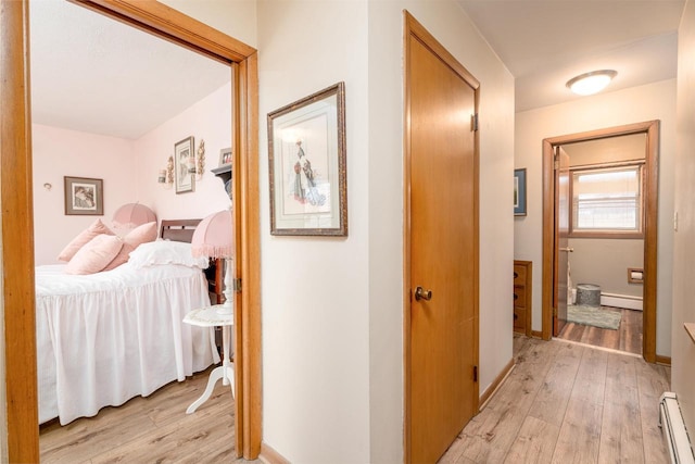 hallway featuring a baseboard radiator, baseboards, and light wood finished floors