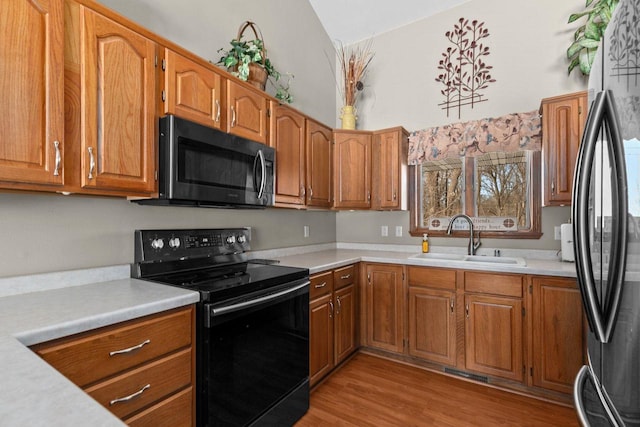 kitchen featuring a sink, light countertops, freestanding refrigerator, black electric range oven, and brown cabinetry