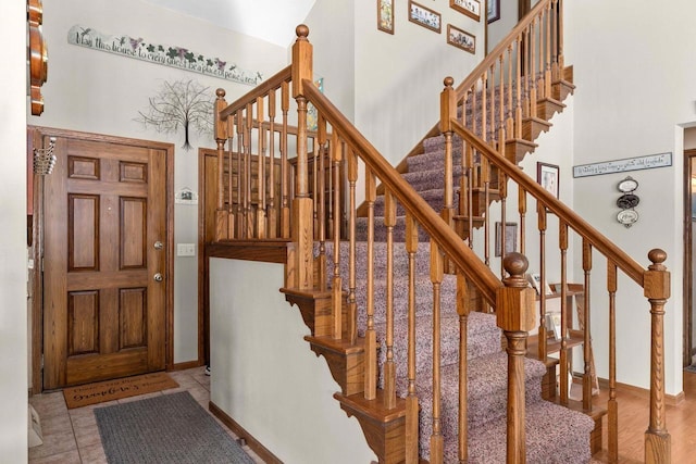 stairs with a towering ceiling, tile patterned flooring, and baseboards