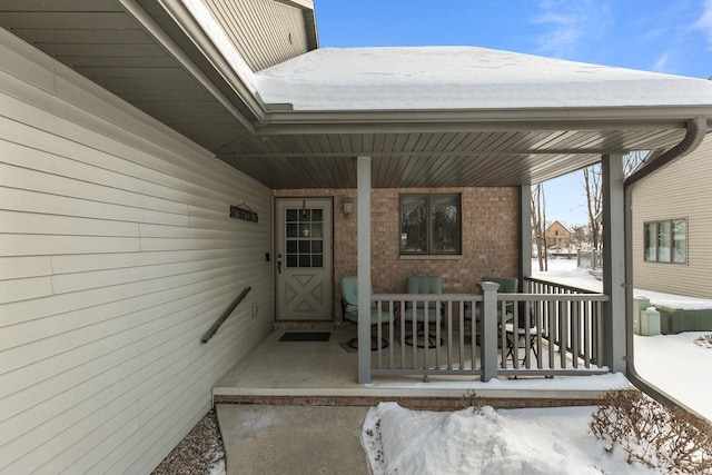 snow covered property entrance with a porch and brick siding