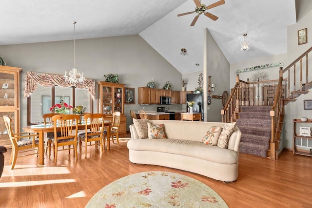 living area featuring light wood-style floors, stairway, high vaulted ceiling, and ceiling fan with notable chandelier