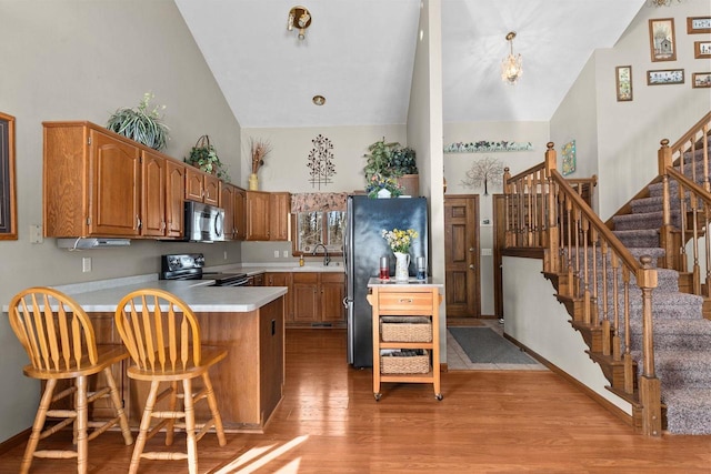 kitchen with high vaulted ceiling, a peninsula, light countertops, appliances with stainless steel finishes, and brown cabinets