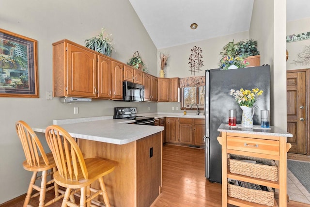 kitchen featuring a breakfast bar area, a peninsula, electric range, light countertops, and brown cabinets