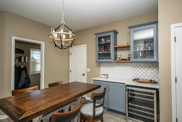 bar with beverage cooler, decorative backsplash, light wood-style flooring, hanging light fixtures, and a chandelier