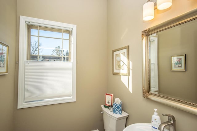 half bathroom featuring toilet, a sink, and a wealth of natural light