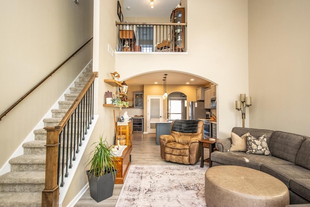 living room featuring arched walkways, light wood-style flooring, a towering ceiling, beverage cooler, and stairs