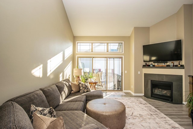 living area with baseboards, a high ceiling, a fireplace, and light wood finished floors