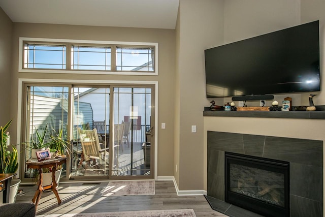 living area with a high ceiling, baseboards, wood finished floors, and a tile fireplace