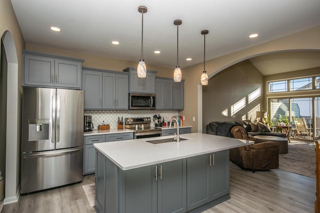 kitchen with pendant lighting, gray cabinets, light countertops, appliances with stainless steel finishes, and a kitchen island with sink