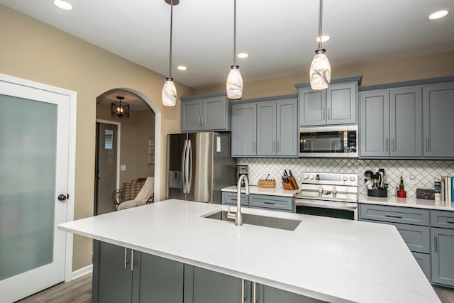 kitchen featuring arched walkways, appliances with stainless steel finishes, hanging light fixtures, light countertops, and a sink