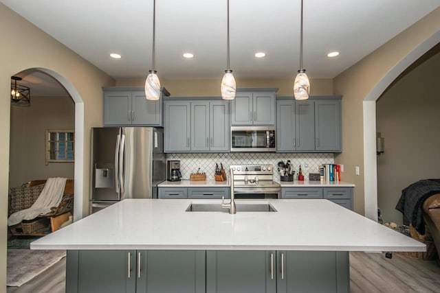 kitchen featuring stainless steel appliances, decorative light fixtures, and an island with sink