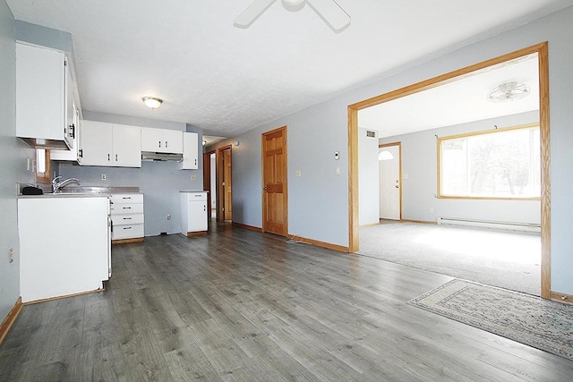 kitchen featuring dark wood-style flooring, white cabinetry, under cabinet range hood, and baseboard heating