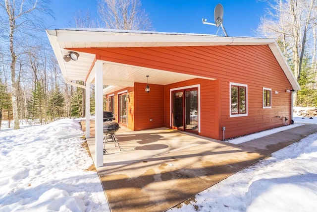 snow covered back of property featuring a patio