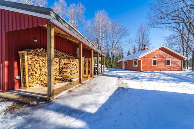 snow covered property featuring a chimney, board and batten siding, and an outdoor structure