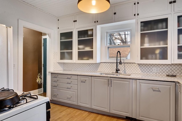 kitchen with white gas range oven, decorative backsplash, glass insert cabinets, light wood-style floors, and a sink