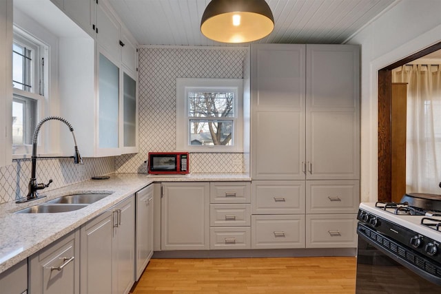 kitchen featuring light wood-style flooring, light stone countertops, a sink, decorative backsplash, and gas range