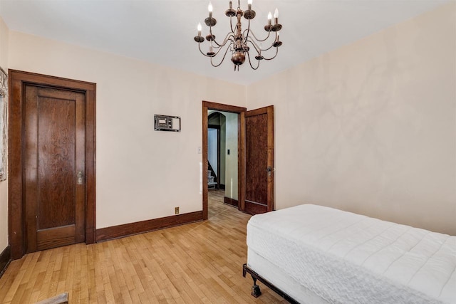 bedroom featuring a notable chandelier, light wood finished floors, arched walkways, and baseboards