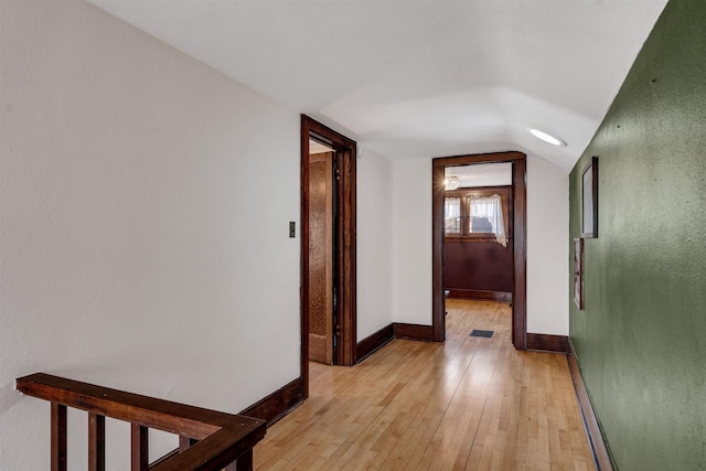 hallway with light wood-type flooring, visible vents, baseboards, and vaulted ceiling