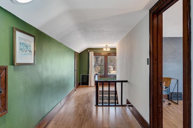 hall with wood-type flooring, vaulted ceiling, and baseboards