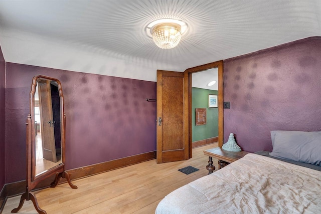 bedroom featuring a notable chandelier, visible vents, baseboards, and wood finished floors