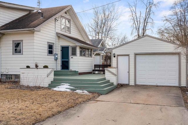 bungalow featuring a shingled roof, concrete driveway, and an outdoor structure