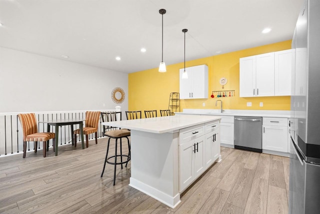 kitchen featuring light wood finished floors, white cabinets, a breakfast bar, light countertops, and stainless steel dishwasher