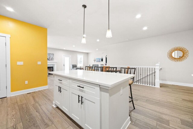 kitchen featuring light wood-type flooring, a kitchen island, white cabinetry, and pendant lighting