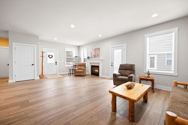 living area with light wood finished floors, baseboards, a glass covered fireplace, and recessed lighting