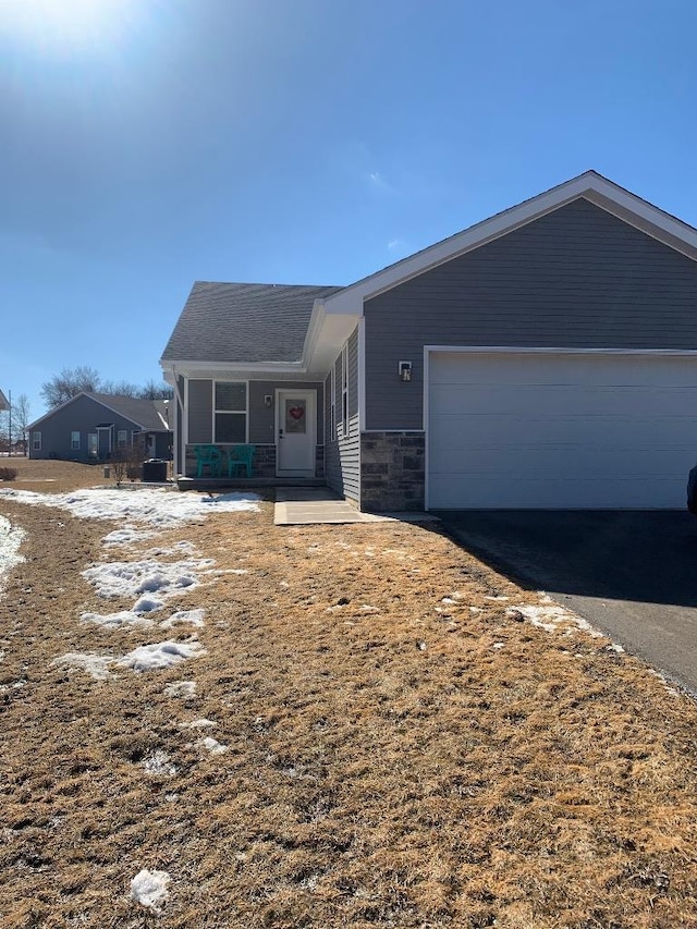 view of front of property featuring an attached garage, stone siding, and aphalt driveway