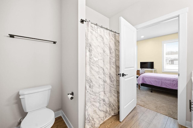 ensuite bathroom featuring a shower with shower curtain, toilet, connected bathroom, wood finished floors, and baseboards