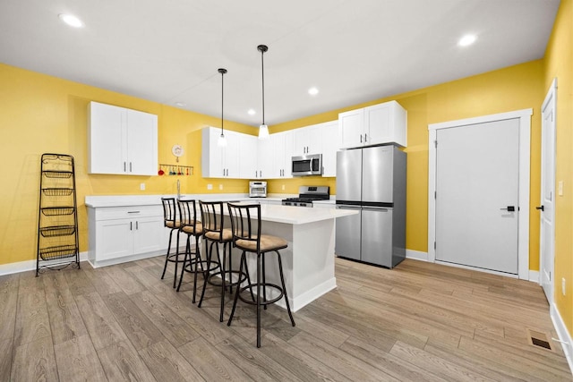 kitchen with a center island, light wood finished floors, stainless steel appliances, light countertops, and a kitchen bar