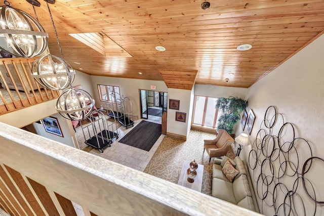 living area featuring vaulted ceiling with skylight, wood ceiling, baseboards, and an inviting chandelier