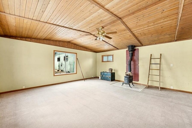 empty room featuring baseboards, ceiling fan, a wood stove, vaulted ceiling, and carpet floors