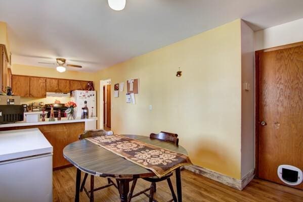 kitchen featuring brown cabinetry, light wood finished floors, refrigerator, light countertops, and white fridge with ice dispenser