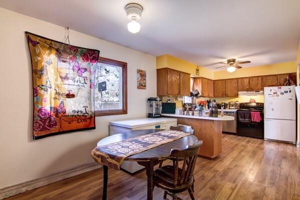 kitchen with light wood-type flooring, black electric range, under cabinet range hood, freestanding refrigerator, and a peninsula