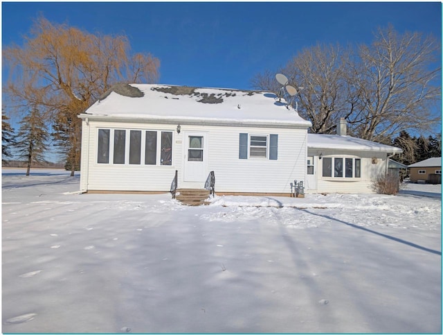 snow covered house with entry steps and a chimney