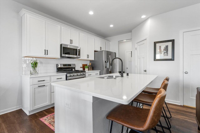 kitchen featuring dark wood finished floors, decorative backsplash, appliances with stainless steel finishes, a sink, and an island with sink