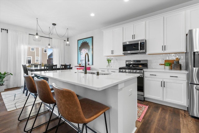 kitchen with decorative backsplash, appliances with stainless steel finishes, a kitchen bar, white cabinetry, and a sink