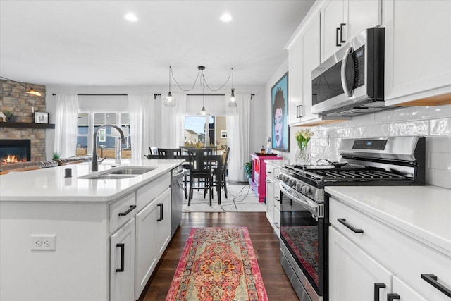 kitchen featuring appliances with stainless steel finishes, a sink, light countertops, a fireplace, and backsplash